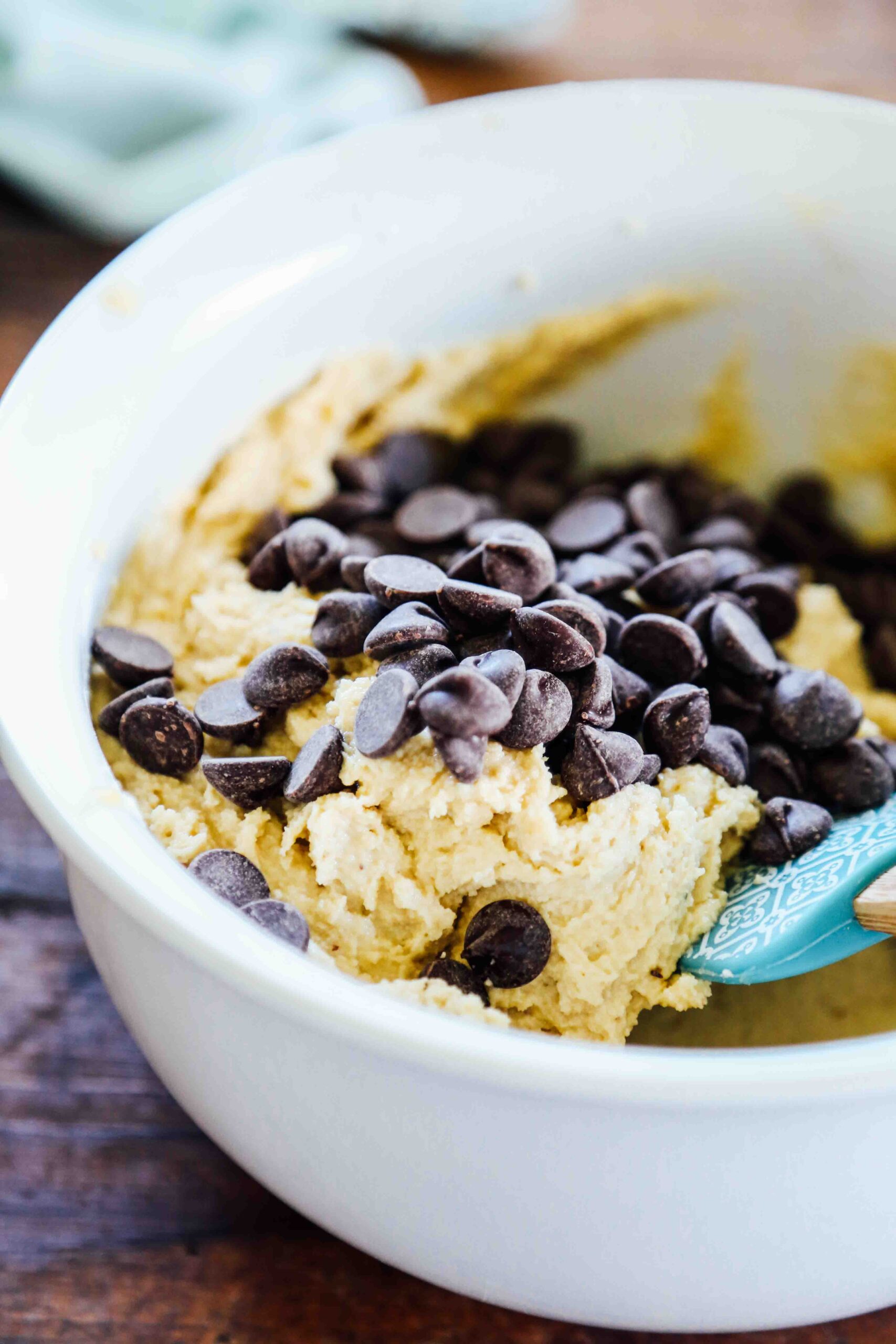 Chocolate chip cookie batter in a large bowl with chocolate chips freshly poured on top.