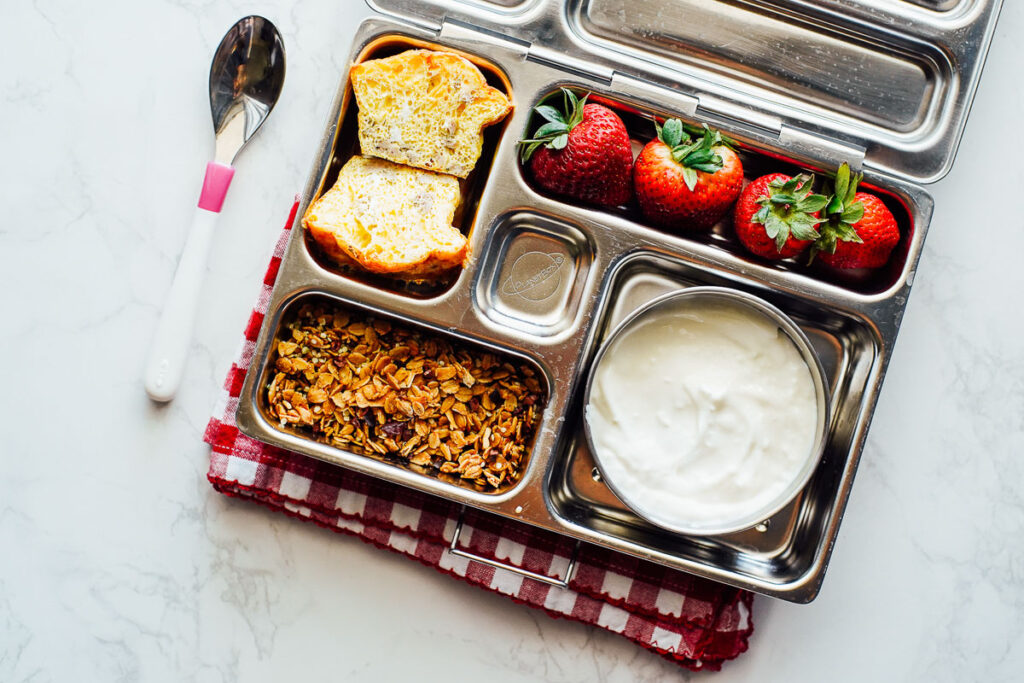 Egg muffin, yogurt and granola, and strawberries in a bento box lunchbox.