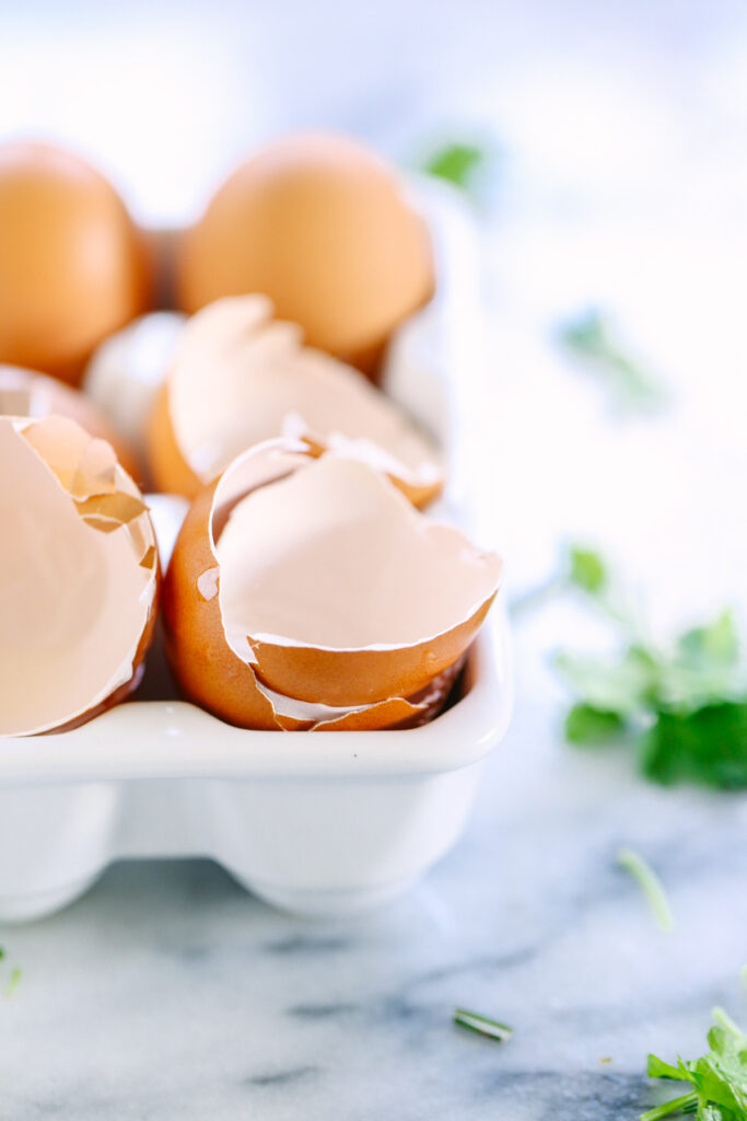 A dozen eggs in a white ceramic egg carton with 2 eggs cracked open.
