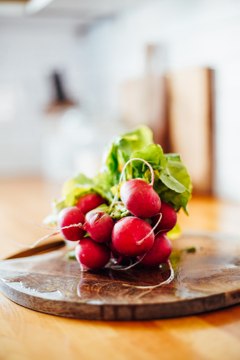 Whole red radishes with the tops on a wooden cutting board in the kitchen.