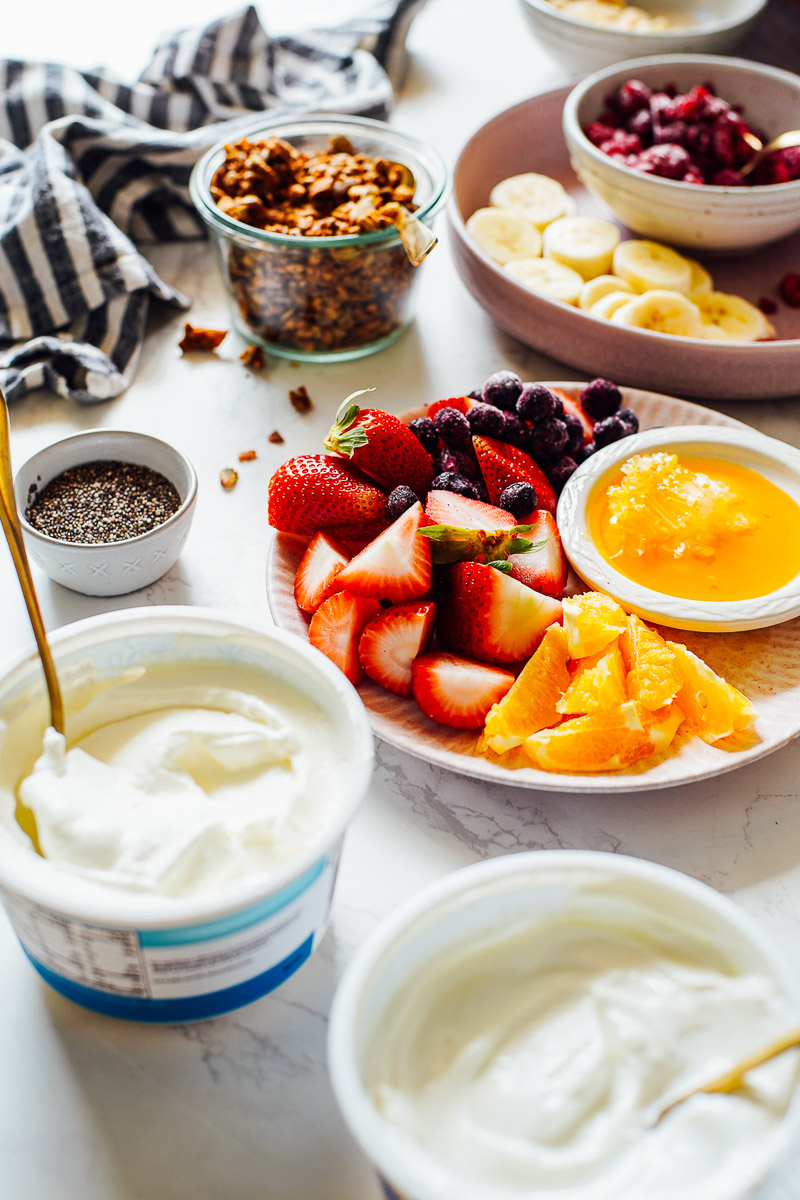 Yogurt, fruit, and granola in bowls on the counter.