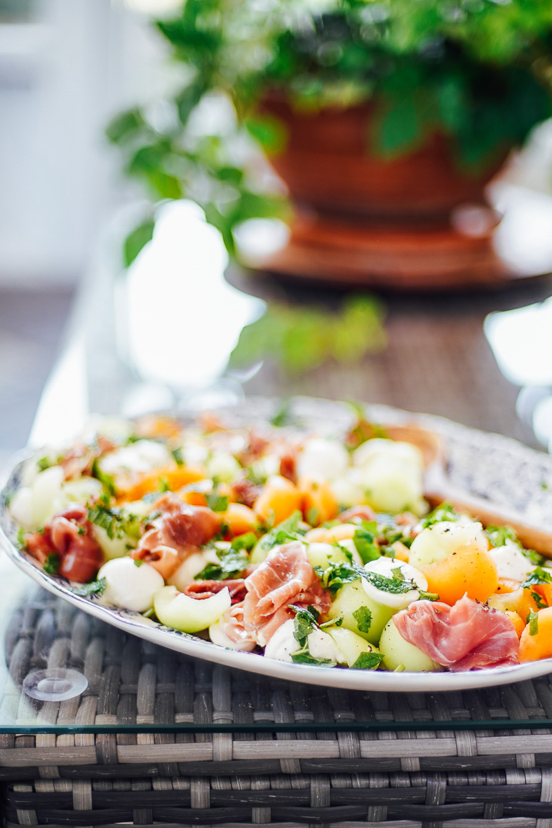 Prosciutto salad with melons on a blue serving platter.