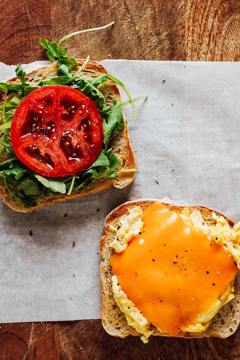 Assembling an egg sandwich: eggs, cheese, arugula, tomato. 