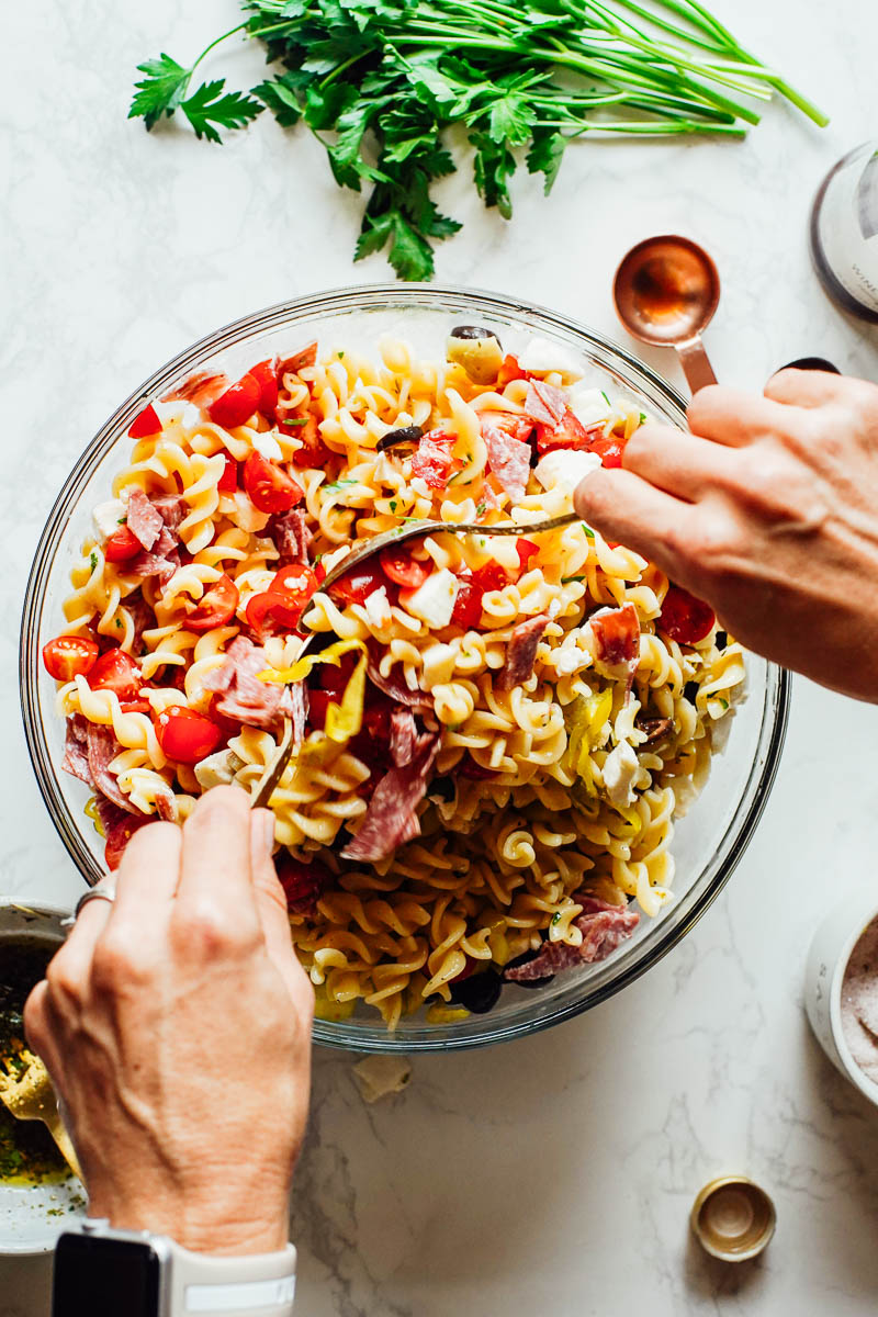 Tossing pasta salad ingredients in a large bowl.